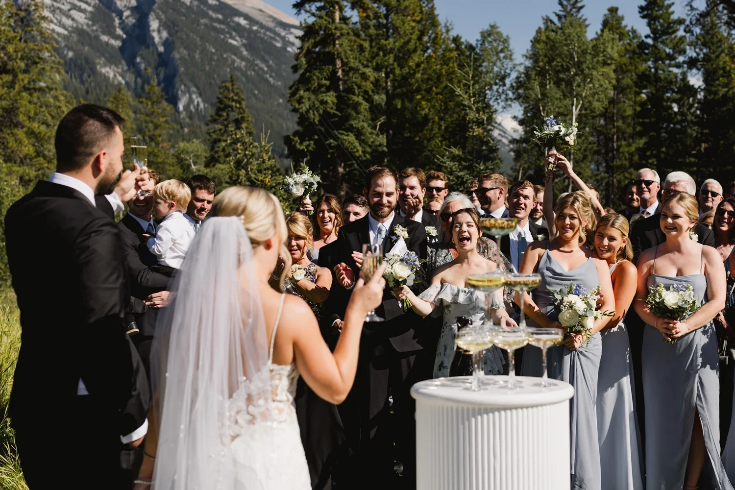 Wedding ceremony outdoors with the bride, groom, and guests celebrating, surrounded by trees and mountains.
