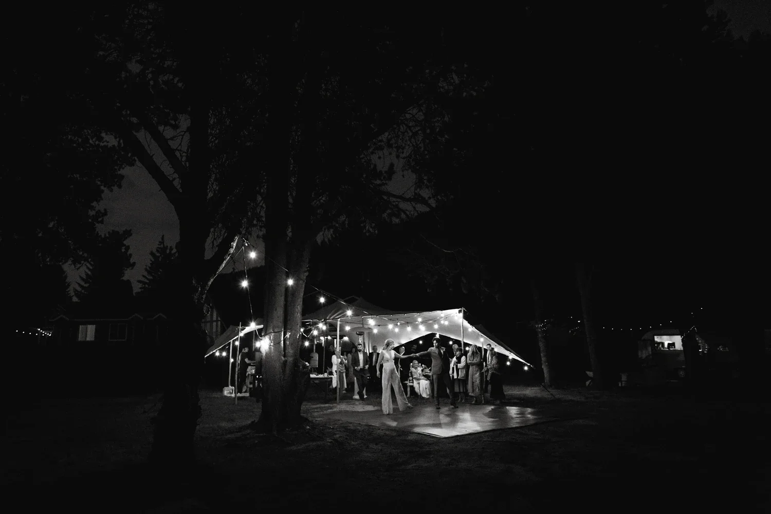 People dancing and socializing under a canopy with string lights at a nighttime outdoor event in a park or backyard.