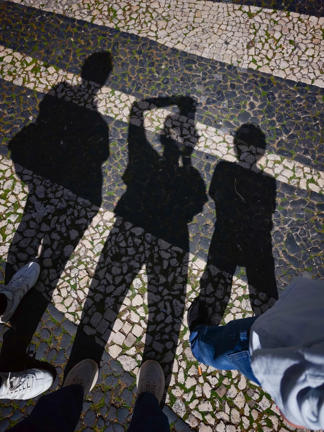 Shadows of four people on a patterned sidewalk, with visible shoes and pants, taken from above at night.