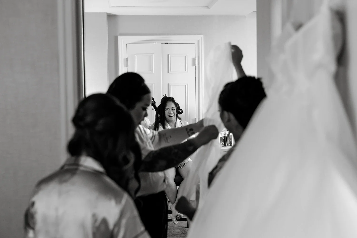 Women getting ready for a wedding, with one woman in the background smiling.
