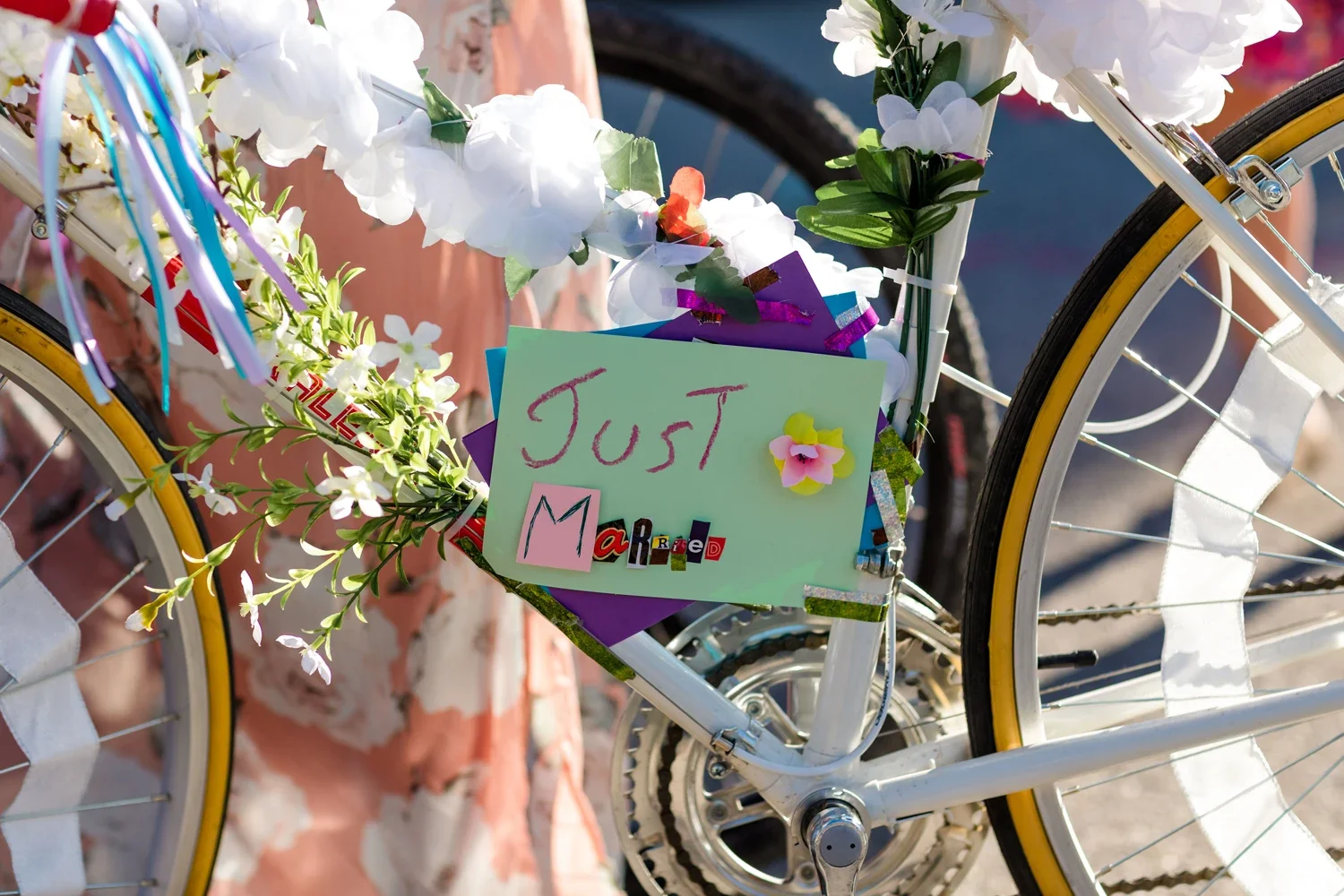 A decorated white bicycle with flowers and a sign that reads 'Just Married' in colorful letters.