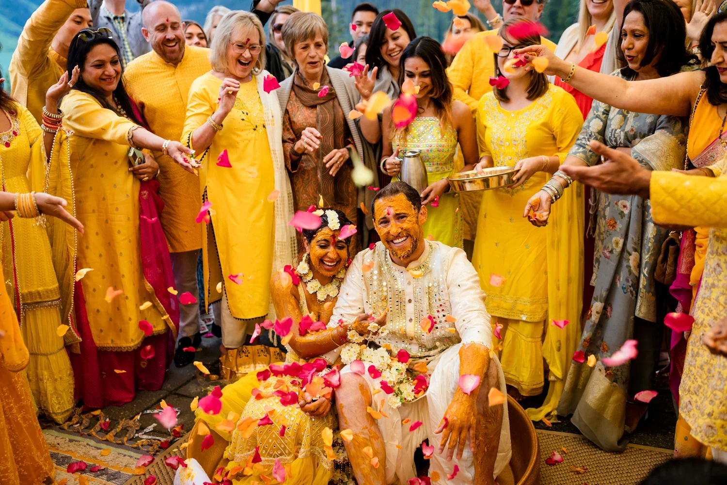 A joyful wedding celebration with the bride and groom dressed in traditional Indian attire, surrounded by friends and family throwing flower petals.