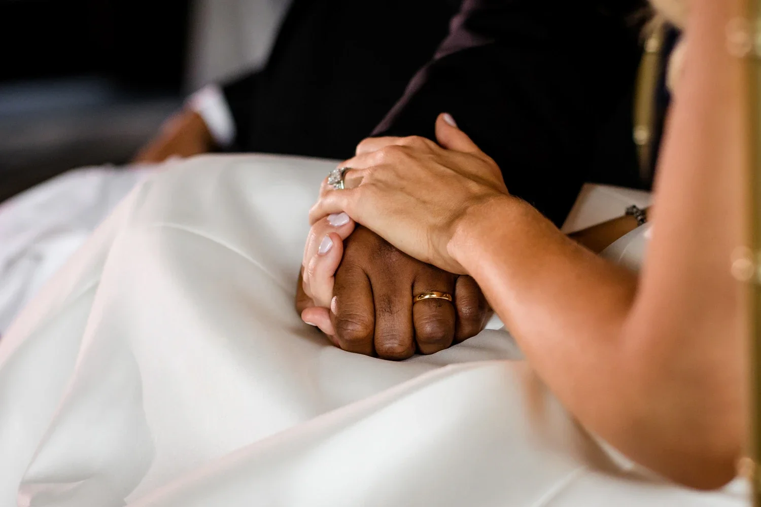 A couple holding hands during a wedding or special occasion, showing rings on their fingers.