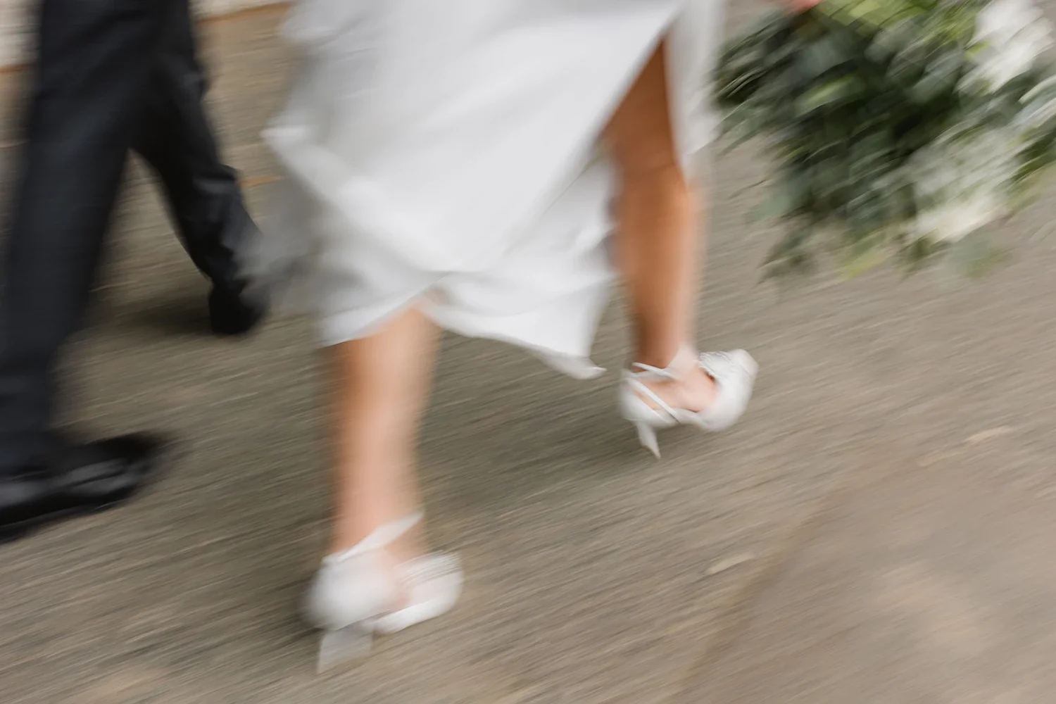 Blurred image of a person walking on a sidewalk, wearing a white dress and white high heels.