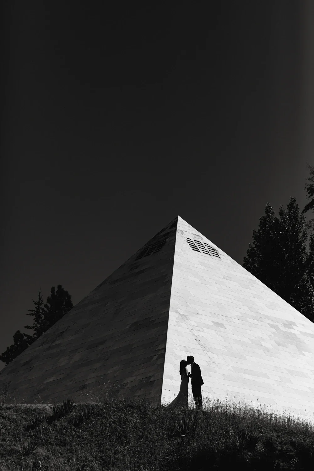 Silhouette of a couple kissing in front of a triangular building during nighttime