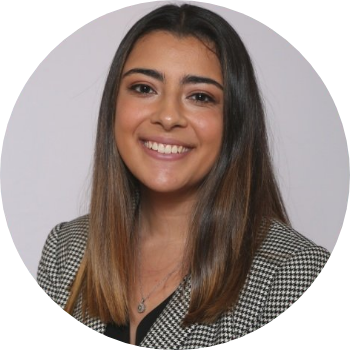 Portrait of a young woman with long brown hair, smiling, wearing a checkered blazer and a necklace.