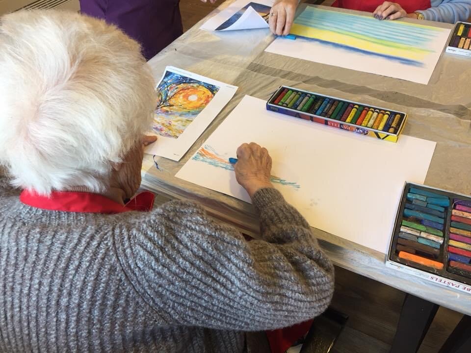 Vicky Steane Art Classes. Elderly person drawing with pastels at a table with art supplies.