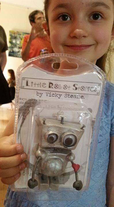Young girl holding "Little Robot Stories" toy in packaging, with a toy robot inside, featuring large eyes and a heart detail.