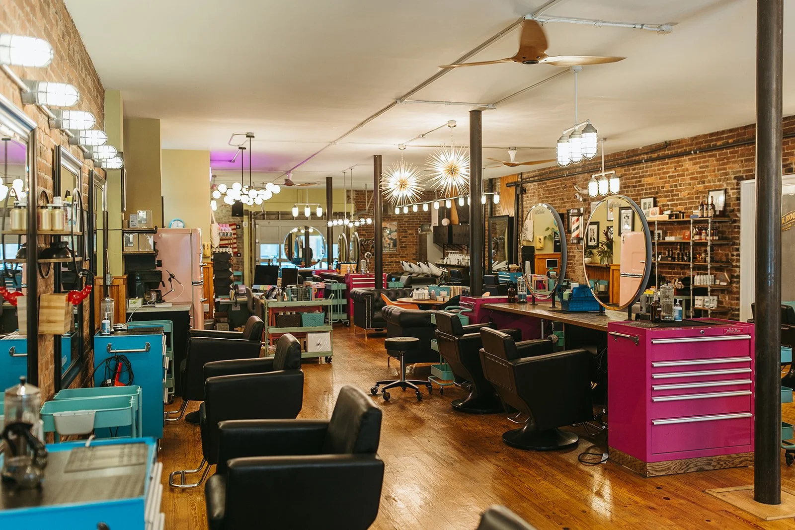 Interior of Cha Cha's with black chairs, mirrors, and colorful styling stations, wood floors, exposed brick walls, and modern light fixtures.