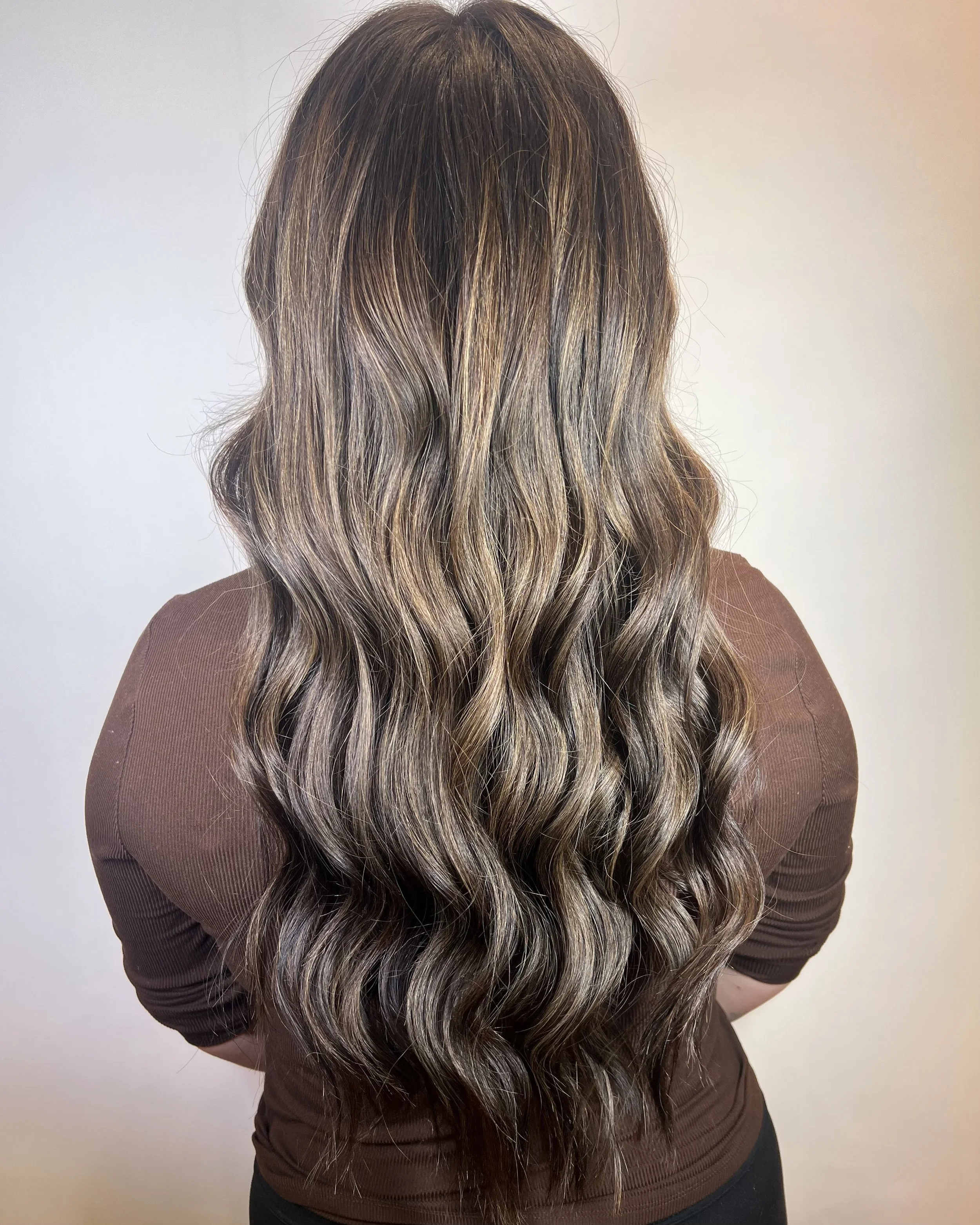 Long wavy hair with balayage highlights on person facing away, wearing a brown top.