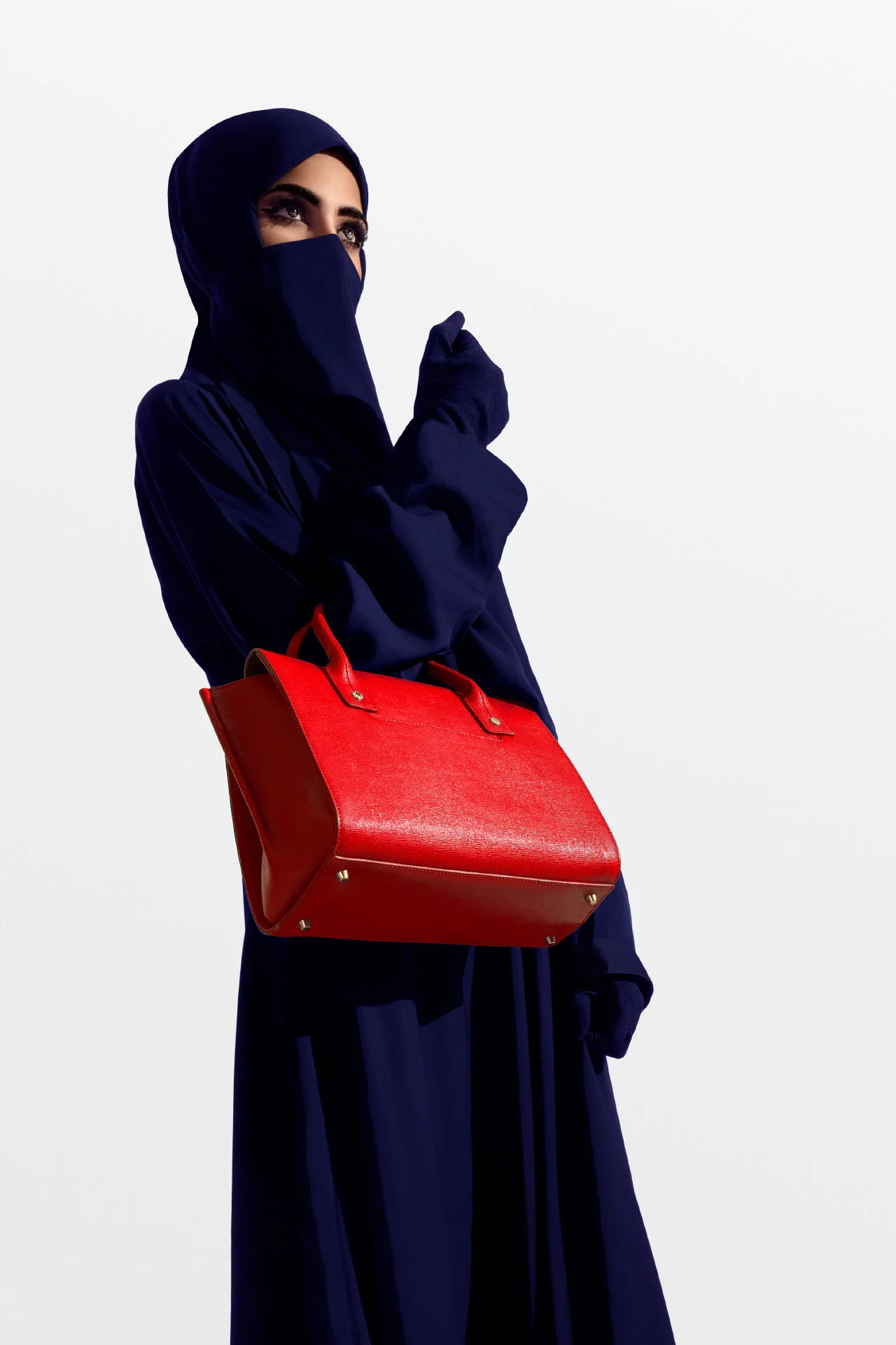 Profile fashion shot highlighting luxury red tote bag and niqab styling in studio lighting by Hammad Iqbal