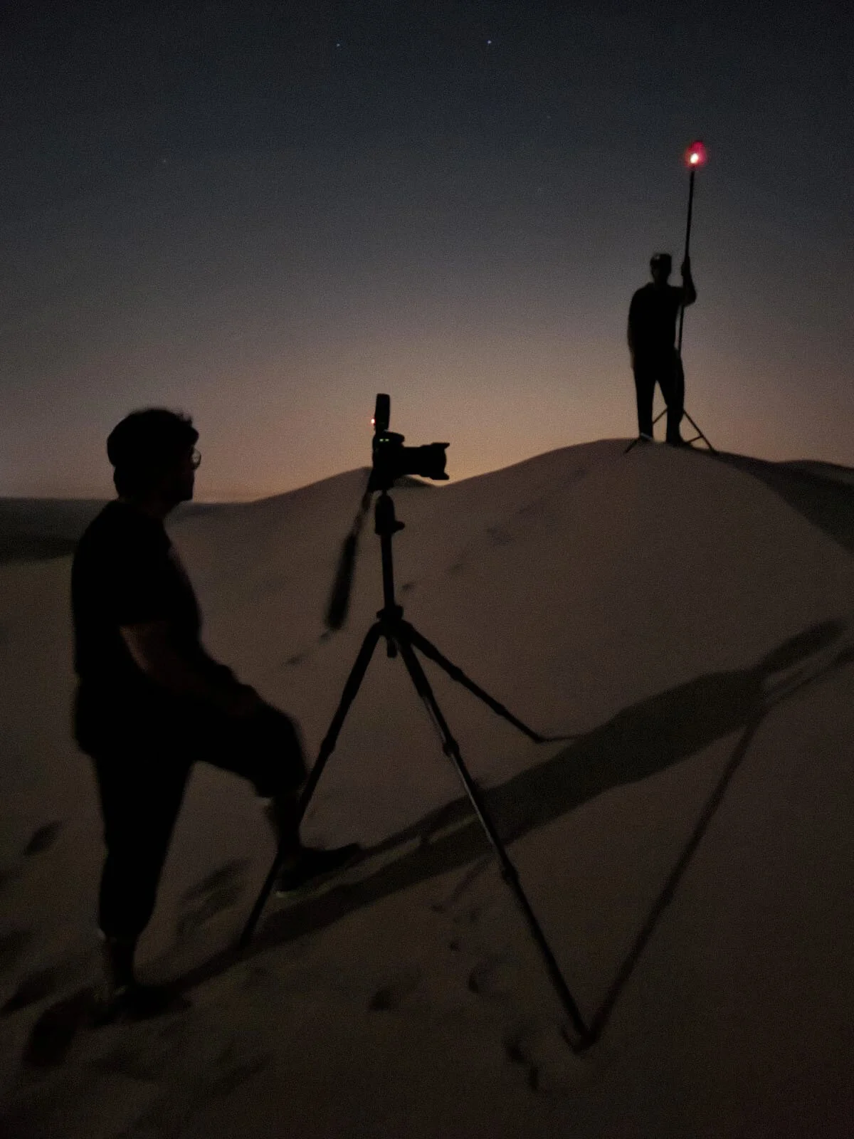 Behind the scenes photo showing camera setup on tripod paired with remote off camera flash on a light stand on a dune ridge