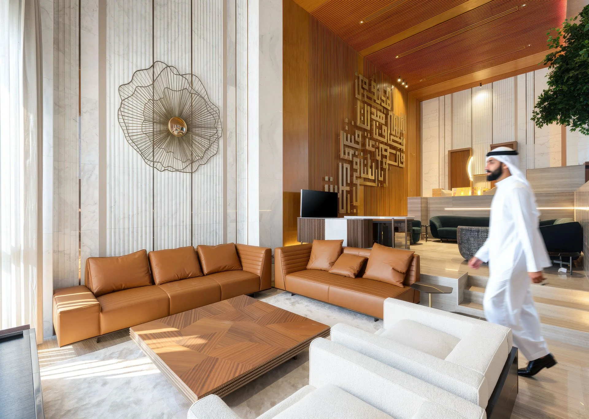 Wide interior architectural view of a luxury split-level living room featuring cognac leather sofas, white marble accent walls, slatted timber ceilings, and a custom Arabic calligraphy wall in a villa at The Pearl Qatar by Hammad Iqbal