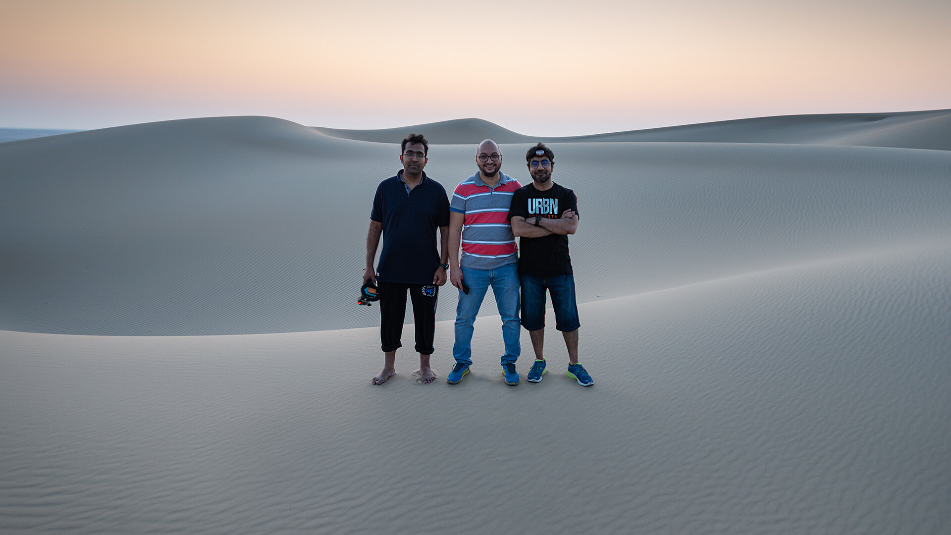 Behind the scenes team group portrait of photographer Hammad Iqbal and crew on sand dunes at dawn after a night photo shoot in Qatar