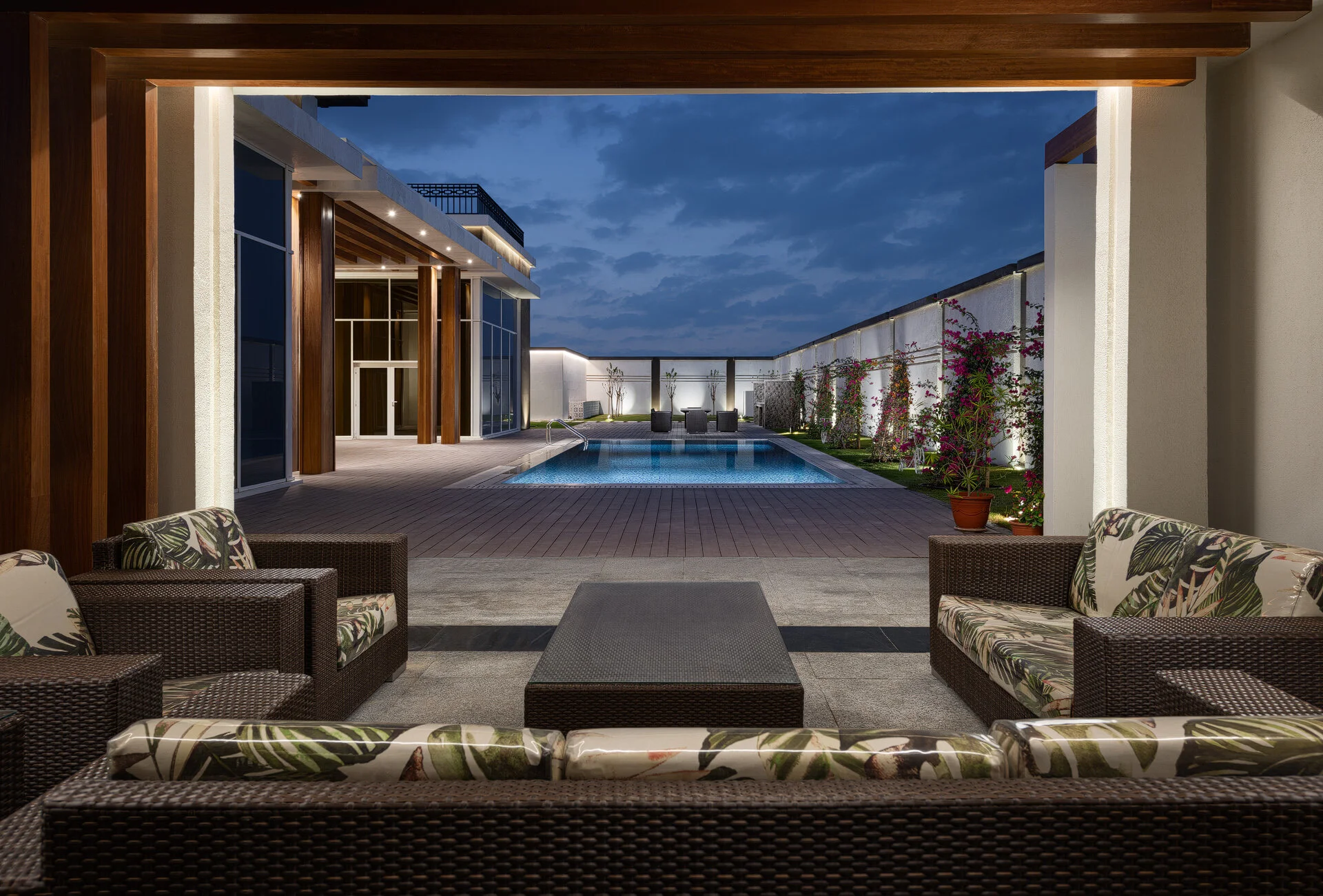 Outdoor courtyard pool terrace at dusk with wicker lounge seating and timber framing in a West Wukair villa photographed by Hammad Iqbal