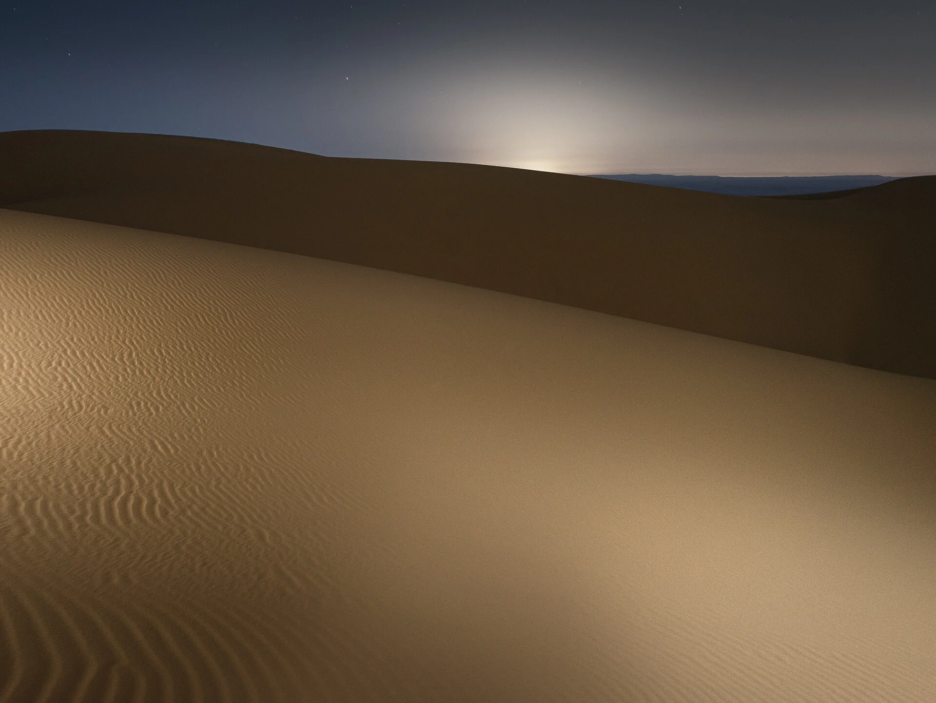Night photography of ambient light rising over an illuminated sand dune crest in Qatar by Hammad Iqbal