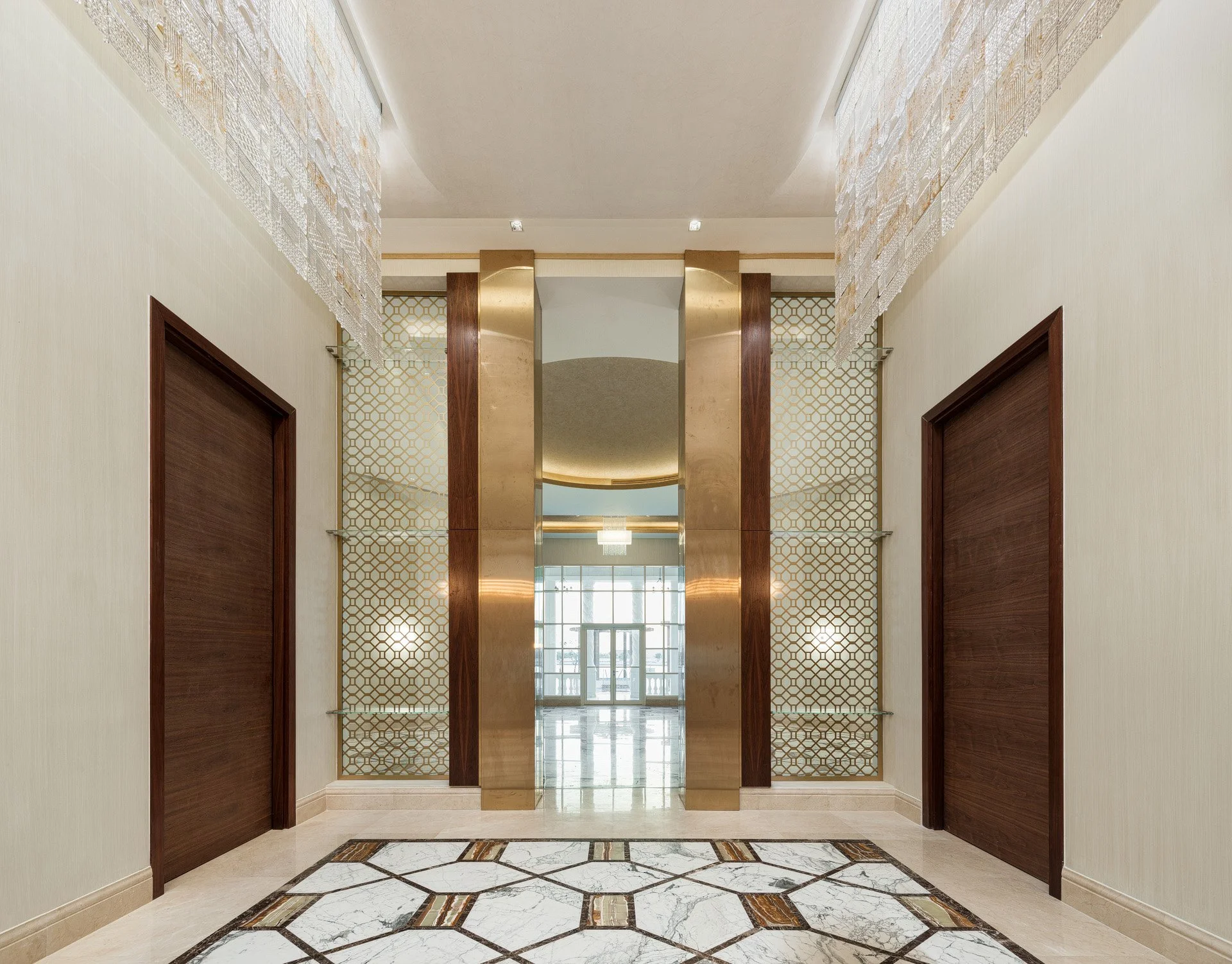 Symmetrical interior view of a luxury villa foyer with geometric marble floor inlay brass accents and hanging crystal chandeliers by Hammad Iqbal