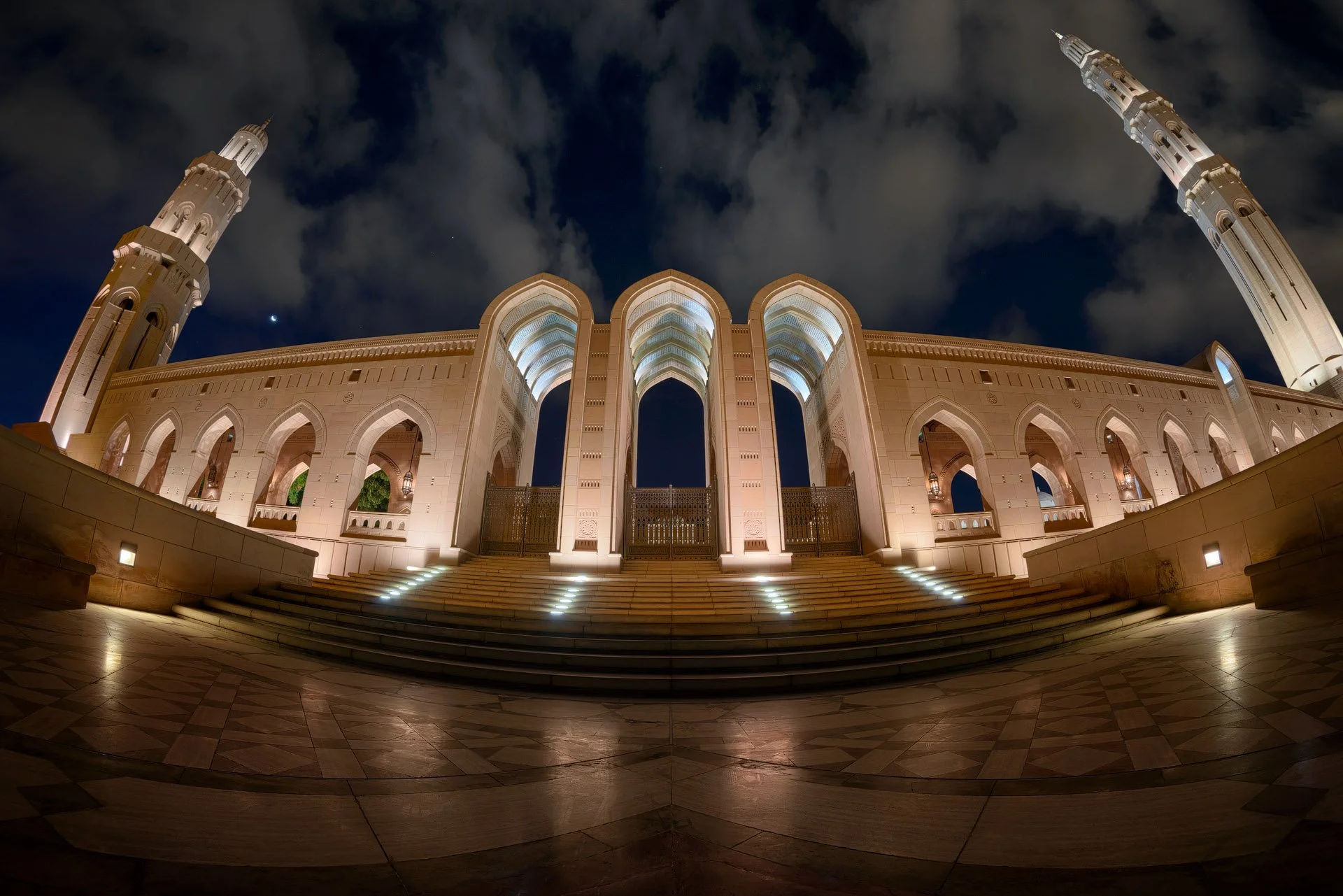 Ultra wide fisheye night photo of the illuminated entrance arches and minarets at Sultan Qaboos Grand Mosque in Muscat Oman by Hammad Iqbal