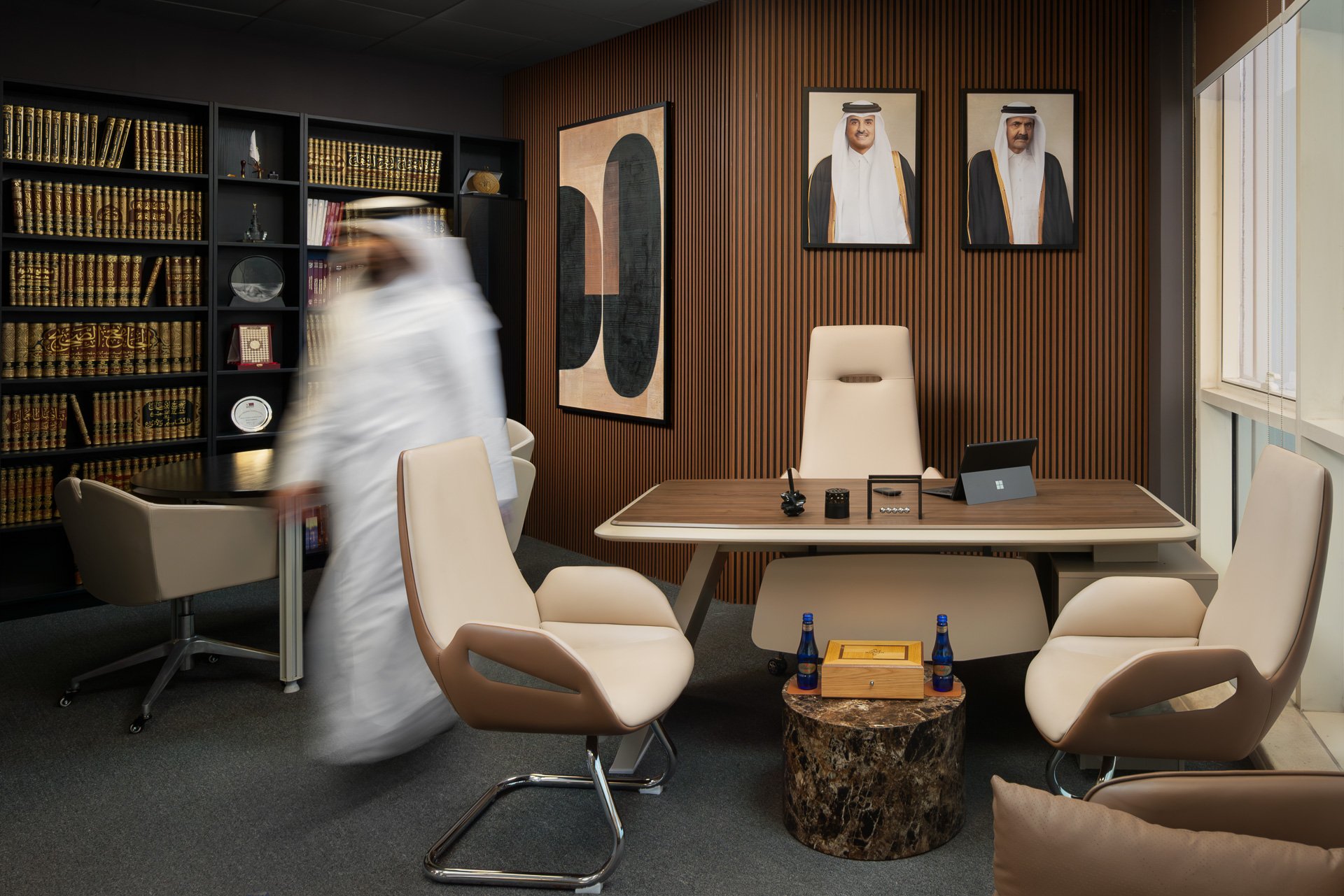 Qatari lawyer walking past executive desk with portraits of Qatari leadership on wooden wall by Hammad Iqbal