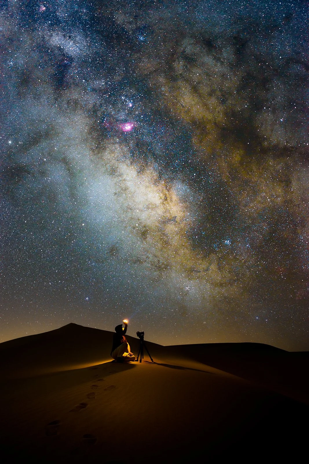 Wide angle astrophotography of bright Milky Way core over sand dunes with photographers in silhouette by Hammad Iqbal