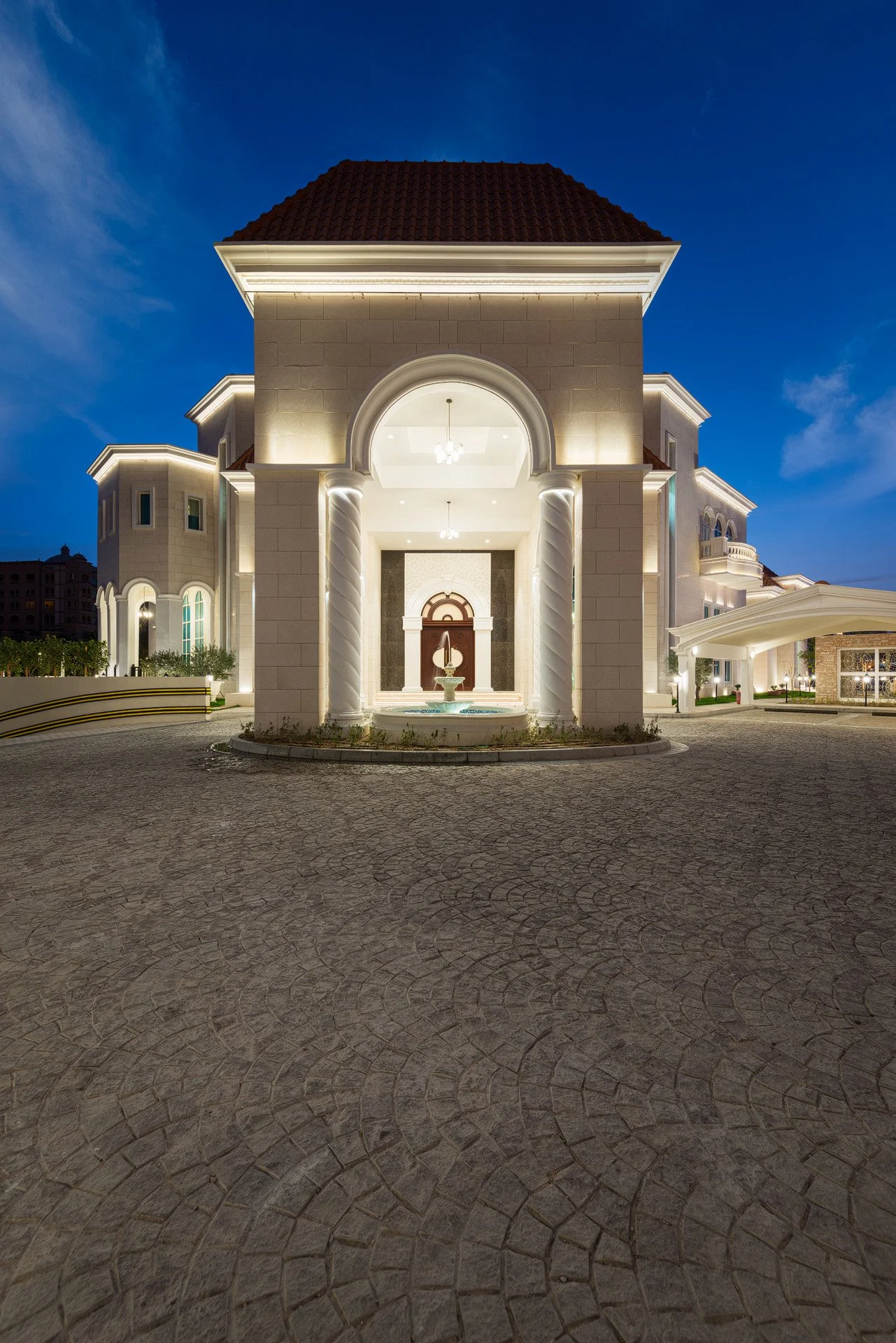 Vertical night photograph of a grand stone entrance archway with illuminated chandelier at a private estate in The Pearl Qatar by Hammad Iqbal