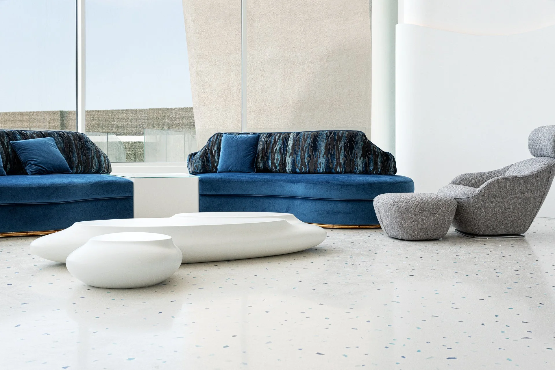 Sculptural organic white pebble coffee tables plush royal blue curved sofas and polished blue terrazzo flooring in a luxury Qatar beach house by Hammad Iqbal