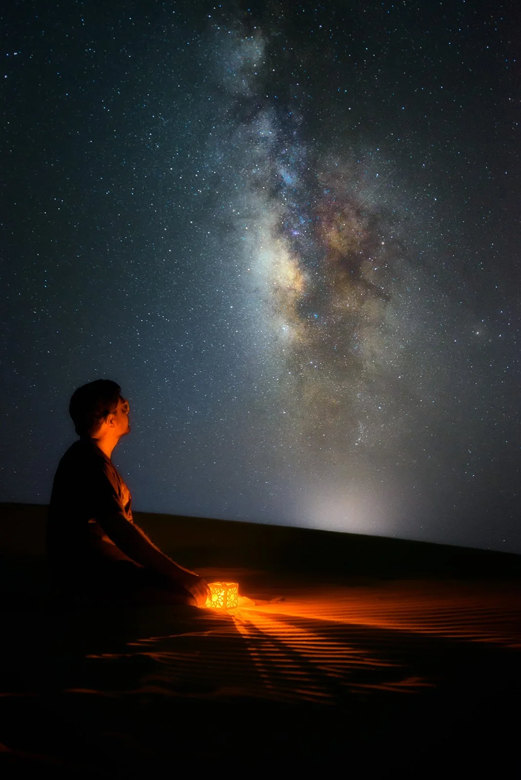 Silhouette of a person seated in contemplation looking up at the bright Milky Way sky in Qatar desert by Hammad Iqbal