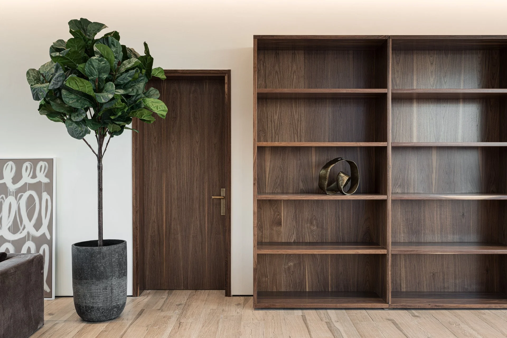 Interior architectural detail of custom dark wood door and open shelving wall unit with potted fiddle leaf fig tree by Hammad Iqbal