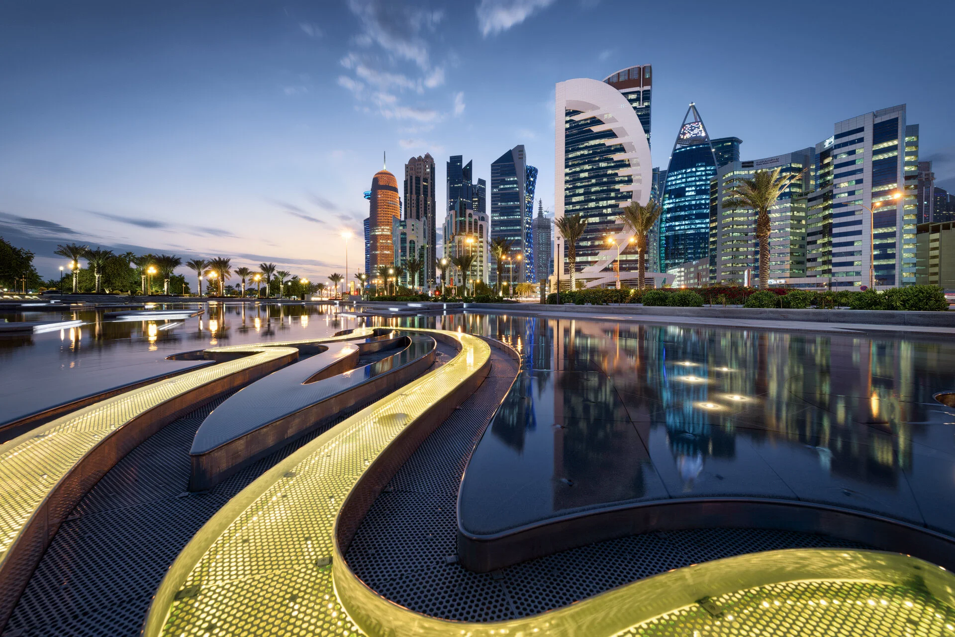 Leading line architectural photo of an illuminated curved bench in the Hotel Park wading pool pointing toward West Bay skyscrapers by Hammad Iqbal