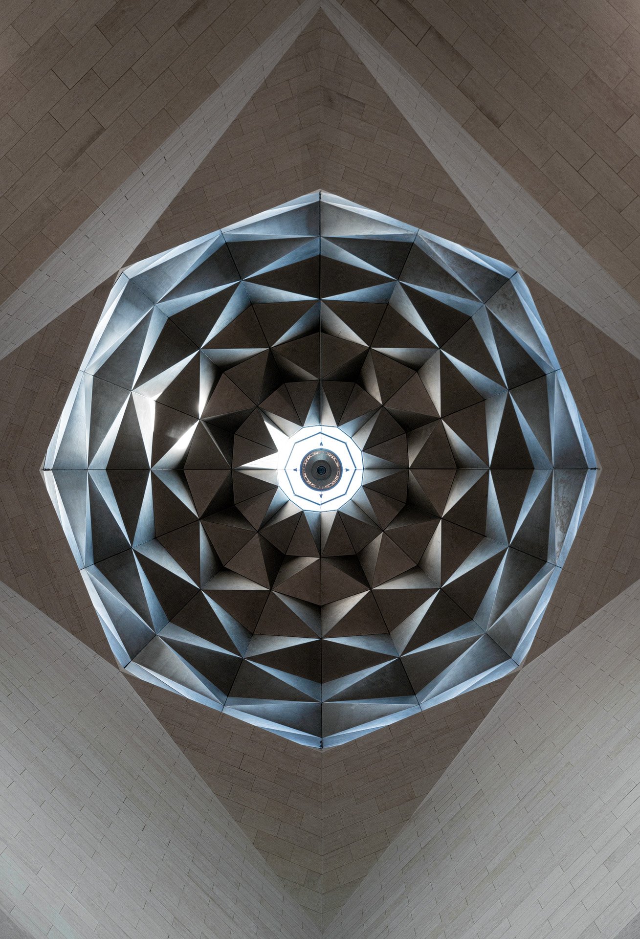 Direct low angle view looking up at the faceted stainless steel dome and central oculus inside the Museum of Islamic Art atrium in Doha by Hammad Iqbal