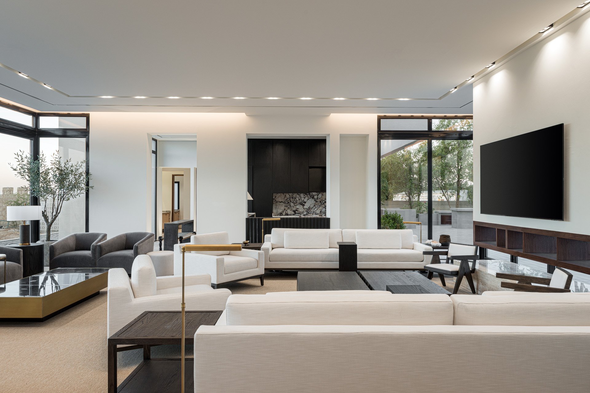 Wide interior view of a luxury entertainment lounge featuring white seating black accent furniture and media wall by Hammad Iqbal