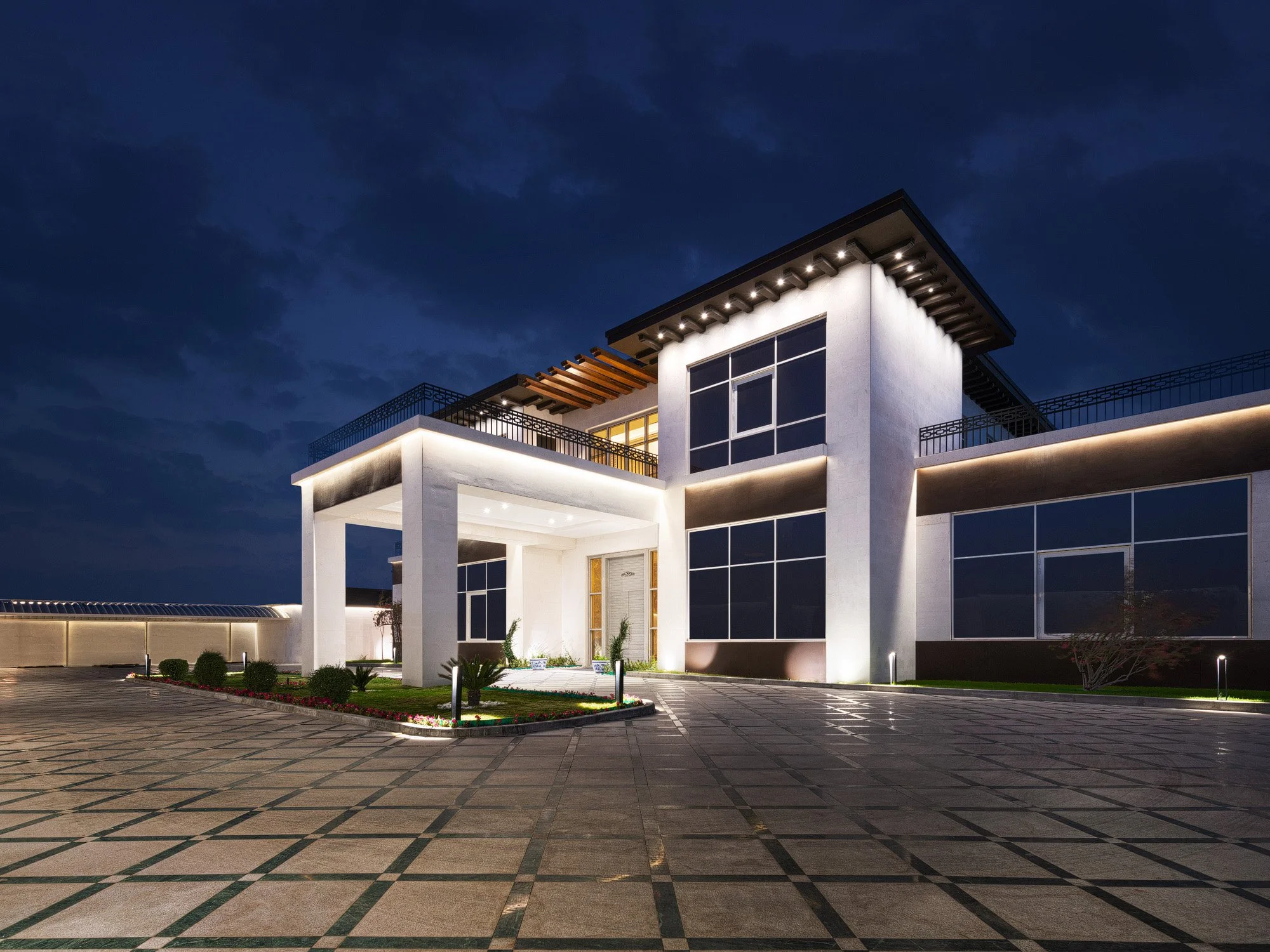 Dynamic night exterior photograph showing the illuminated modern facade and geometric paved driveway of a West Wukair estate by Hammad Iqbal