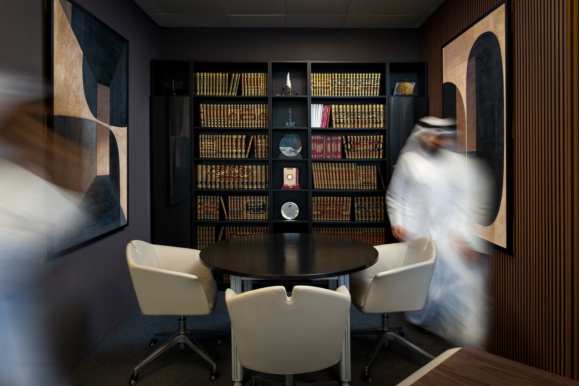 Architectural photo of a private law firm consultation room with built in bookshelves abstract art and moving blurred figures by Hammad Iqbal
