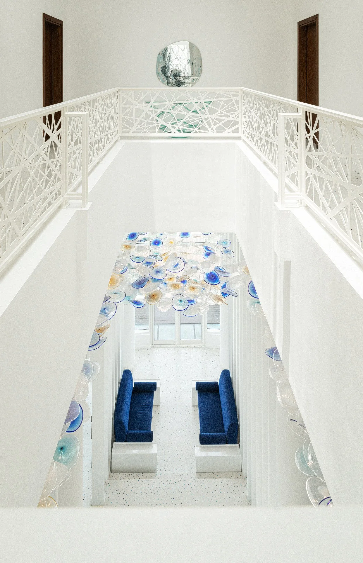 High angle photo looking down a white atrium with custom blue blown glass hanging art installation by Hammad Iqbal