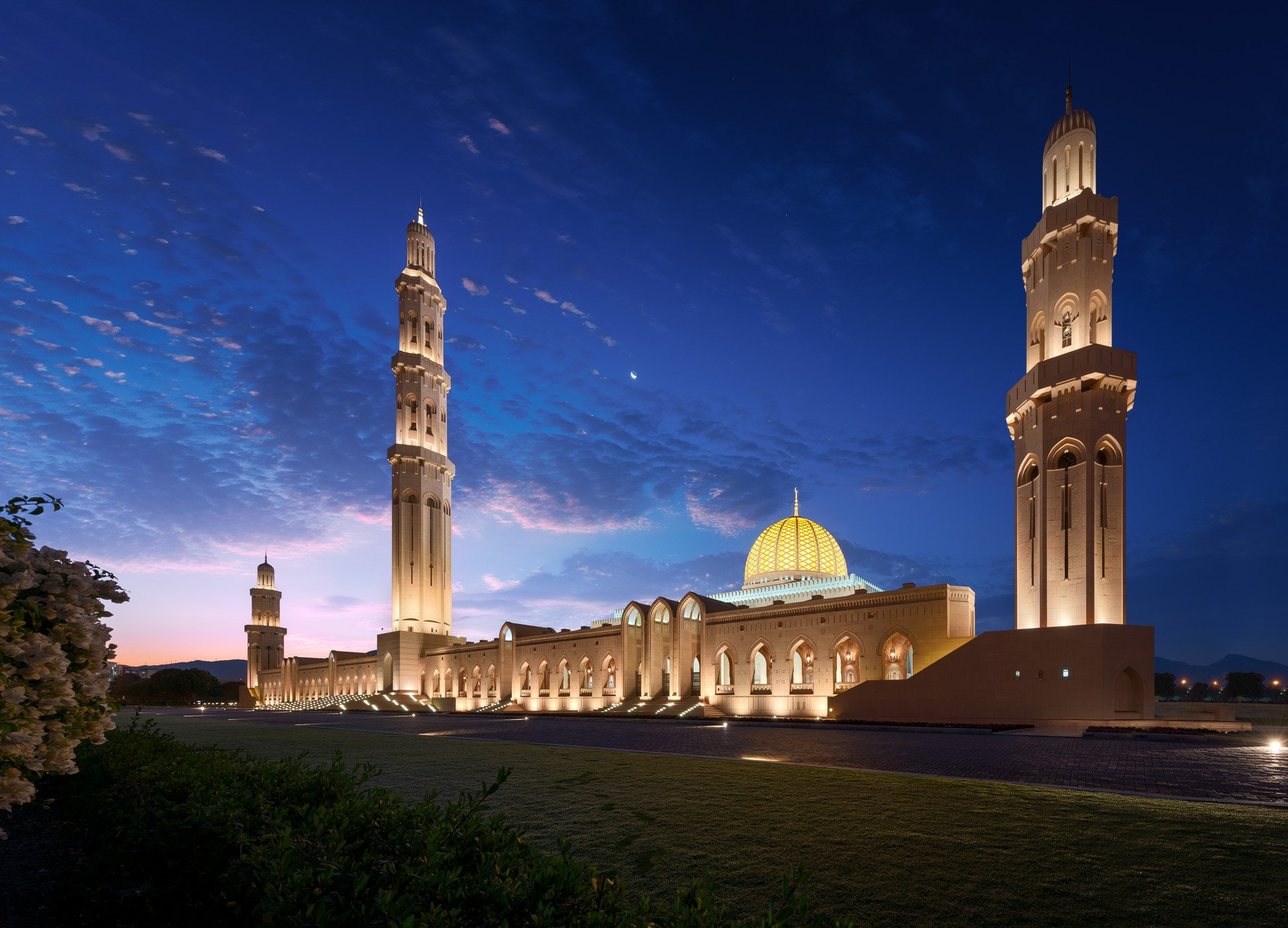 Wide blue hour architectural photo of the illuminated golden dome and minarets at the Sultan Qaboos Grand Mosque in Muscat Oman by Hammad Iqbal