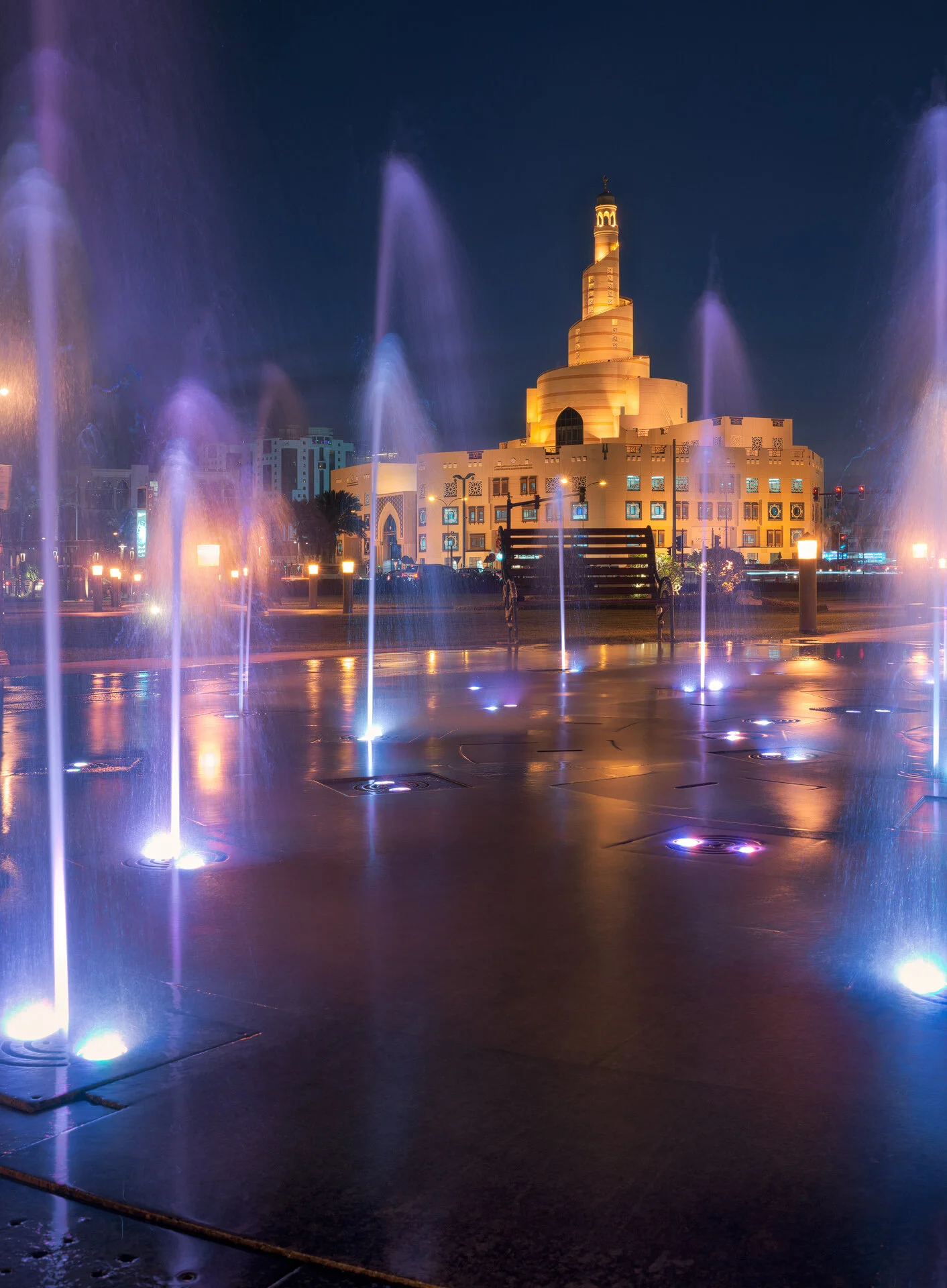 Vertical night photograph of the illuminated Fanar spiral minaret and purple lit fountains in Doha Qatar by Hammad Iqbal
