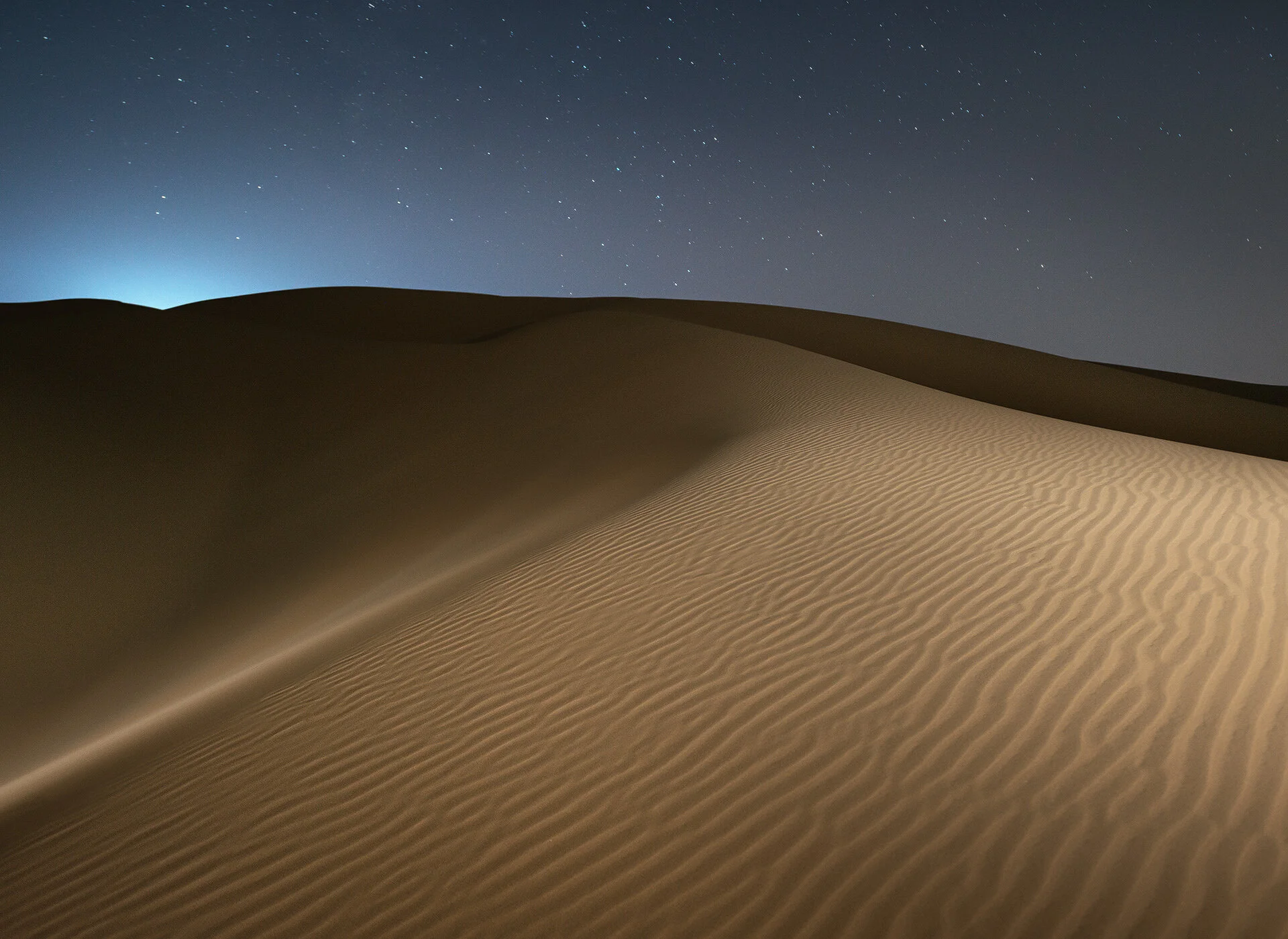 Curved sand dune ridge line silhouetted against a deep blue starlit sky in Qatar by Hammad Iqbal