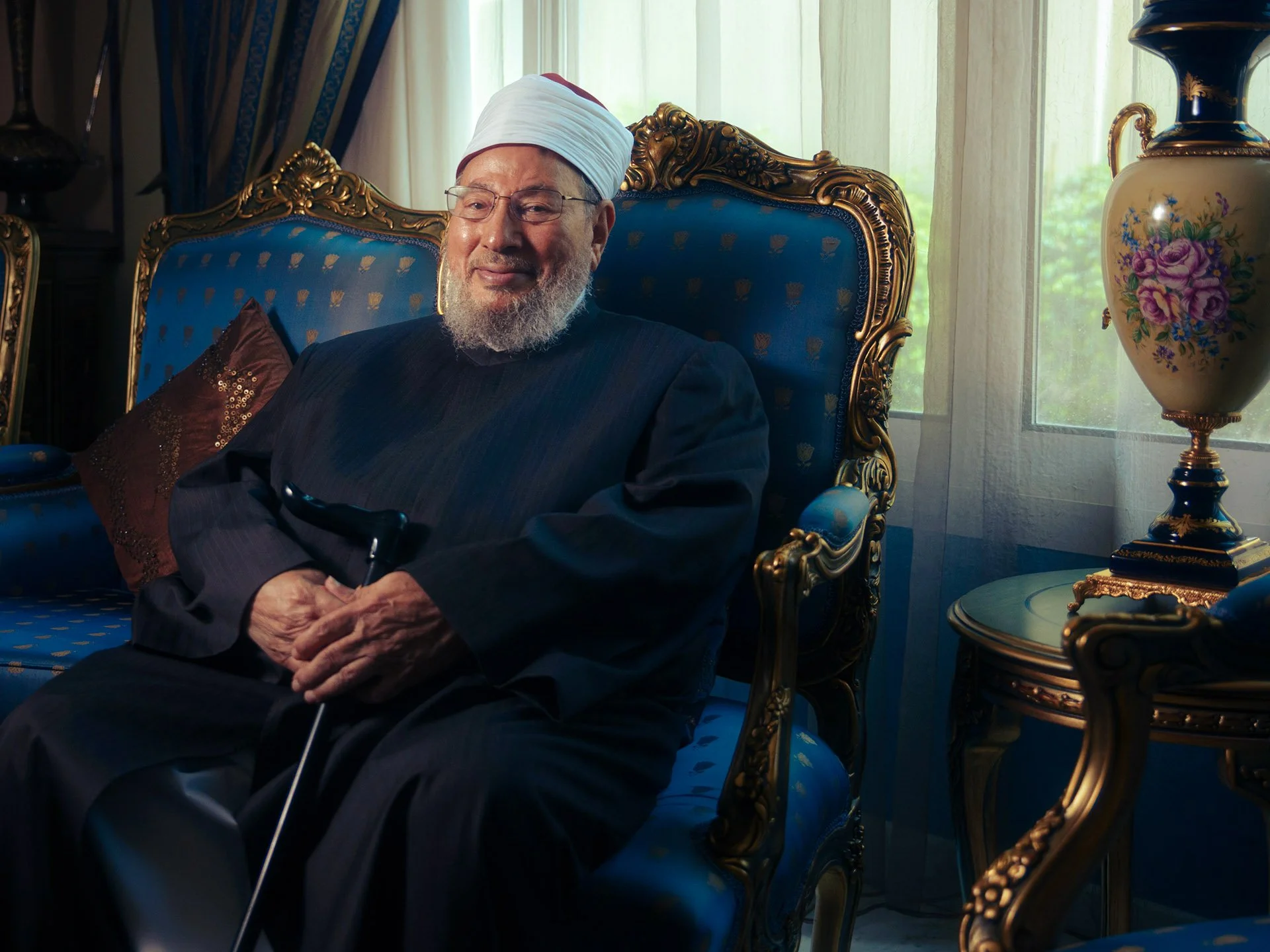 Portrait of Sheikh Yusuf Al-Qaradawi holding a walking cane while seated in an ornate blue armchair by Hammad Iqbal