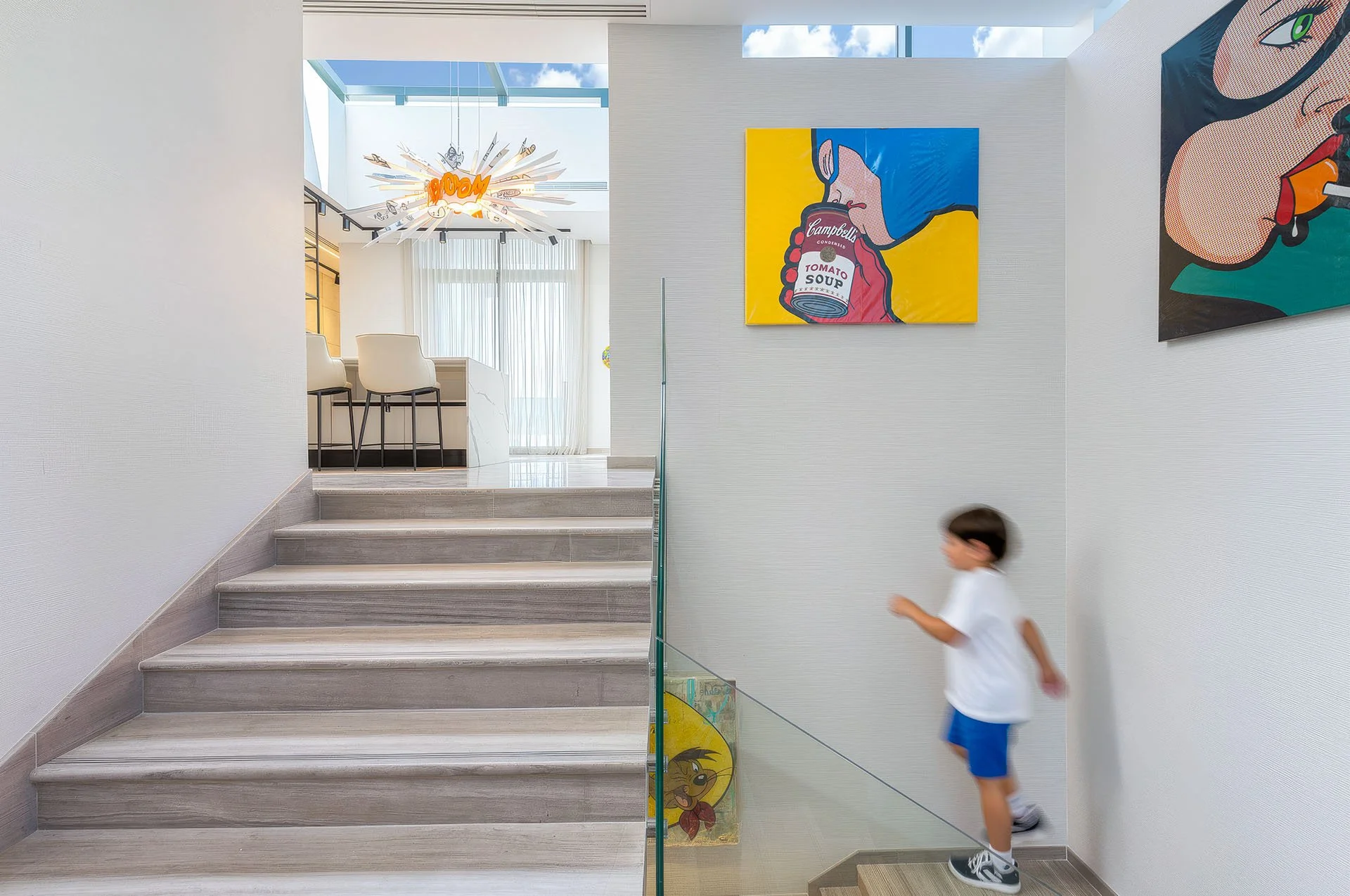 Sunlit stairwell landing with skylight glass and vibrant modern pop art paintings by Hammad Iqbal