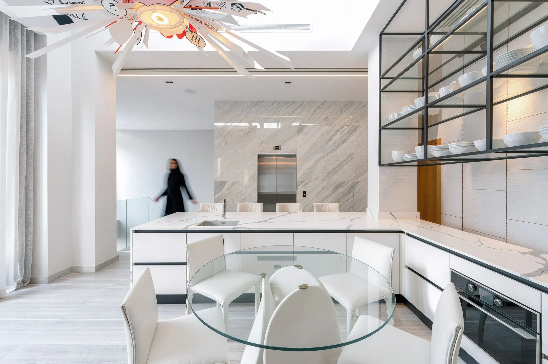 Bright minimalist white kitchen design with central island and glass shelving display in Doha villa by Hammad Iqbal