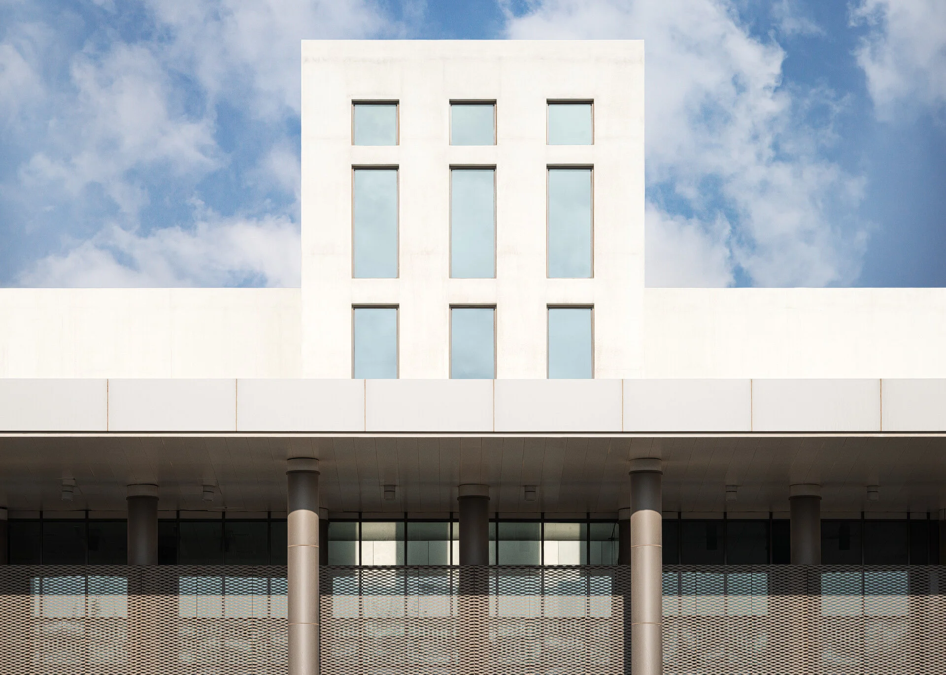 Symmetrical exterior view of the Anti-Doping Lab Qatar building in Aspire Zone showing modern white architectural elevation and structural columns against a blue sky.