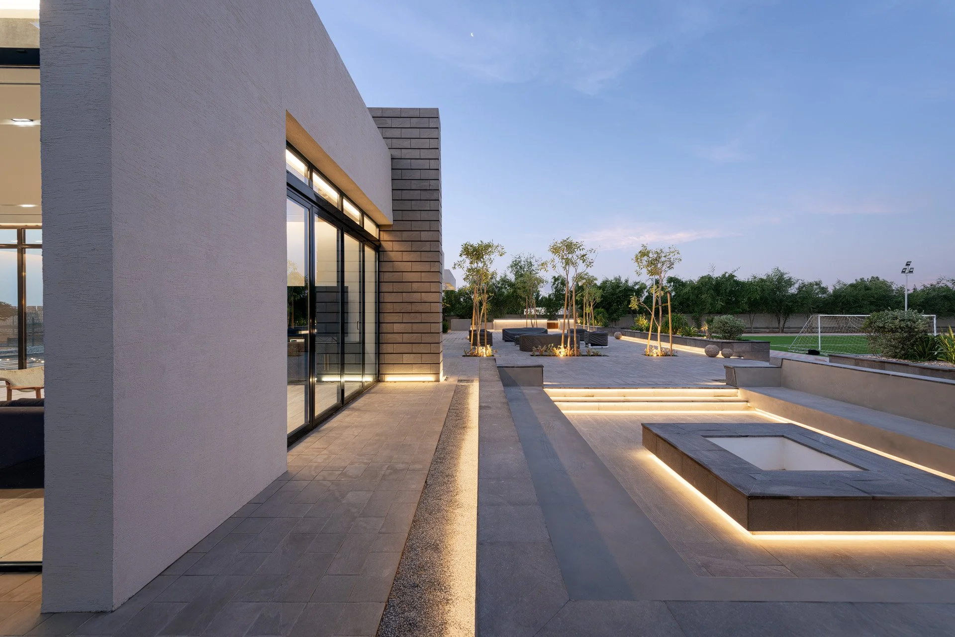 Dusk photo of multi level stone courtyard with sunken fire pit and linear LED strip lighting at a Qatar residence by Hammad Iqbal