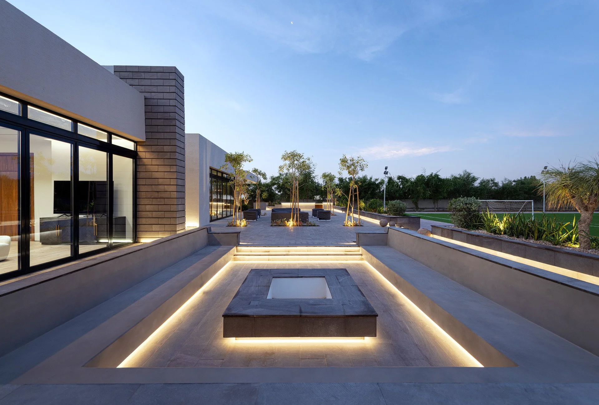 Symmetrical twilight shot of a sunken stone fire pit feature with glowing recessed LED strip lighting in Qatar by Hammad Iqbal