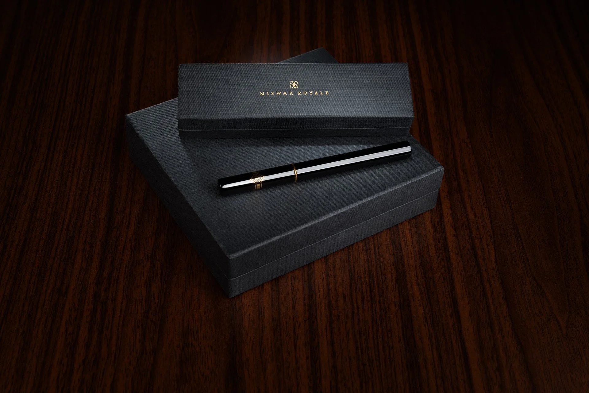 Product packaging shot featuring stacked Miswak Royale boxes and single black case on polished mahogany wood by Hammad Iqbal