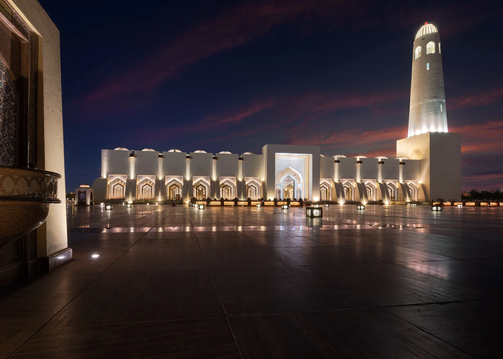 Wide late blue hour photograph of the illuminated Imam Muhammad bin Abdul Wahhab Mosque facade and minaret at twilight in Doha Qatar by Hammad Iqbal
