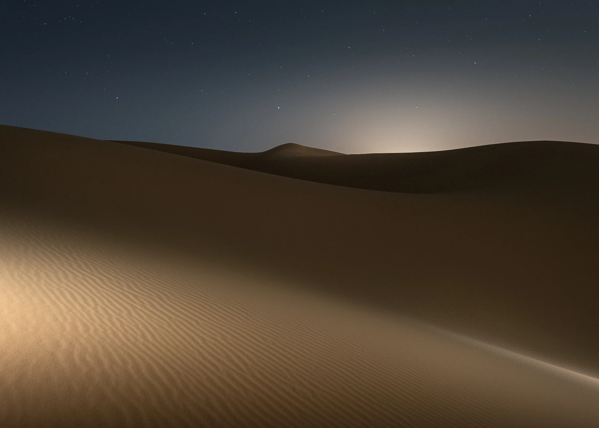 Softly illuminated desert dune saddle showing warm sand tones against night darkness by Hammad Iqbal