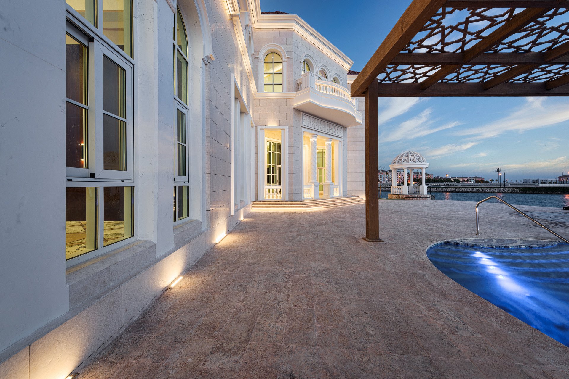 Side terrace view showing warm stone floor lighting wooden pergola and infinity pool at a luxury villa in Doha by Hammad Iqbal