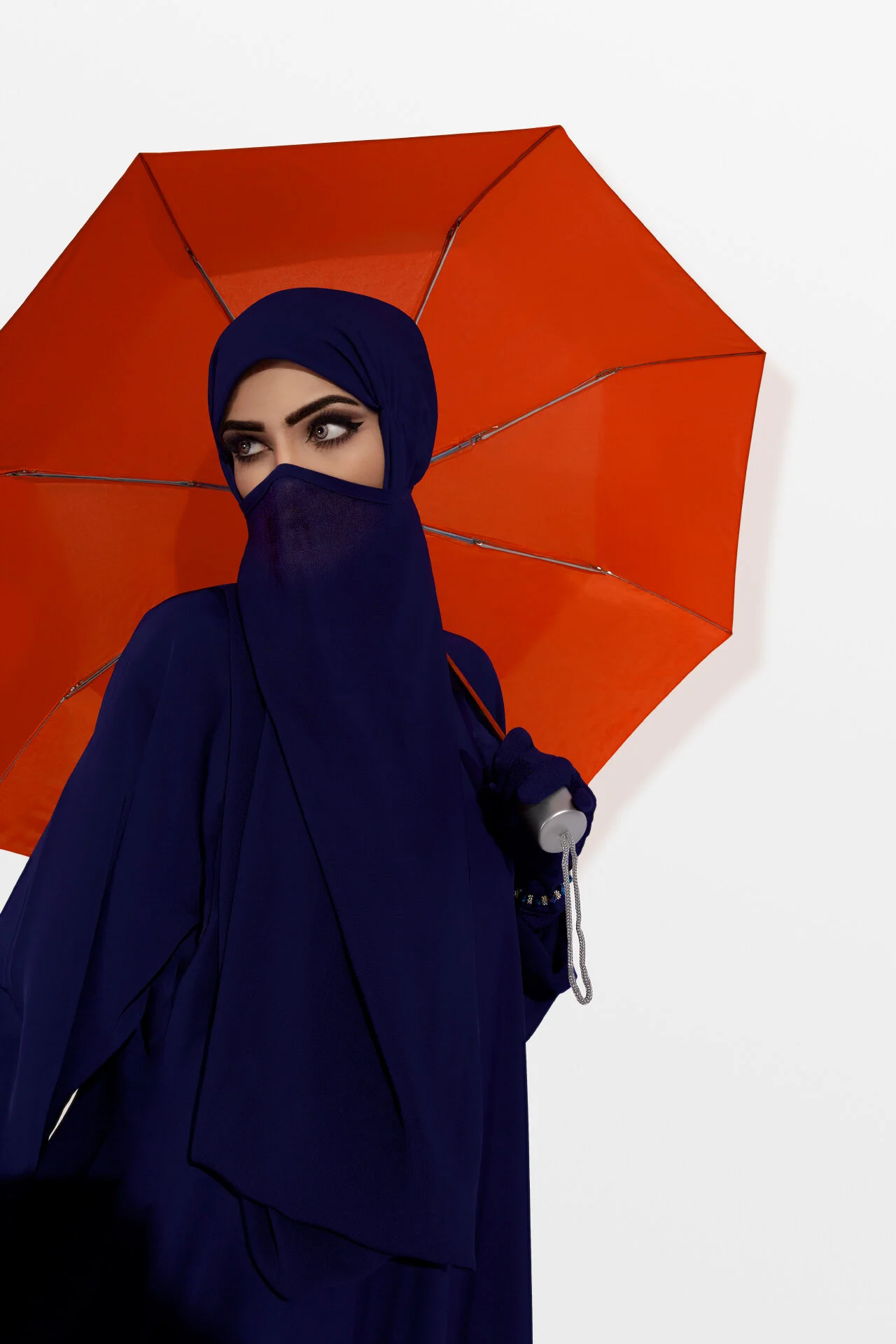 Medium fashion shot of model in navy blue niqab holding a bright orange umbrella by Hammad Iqbal