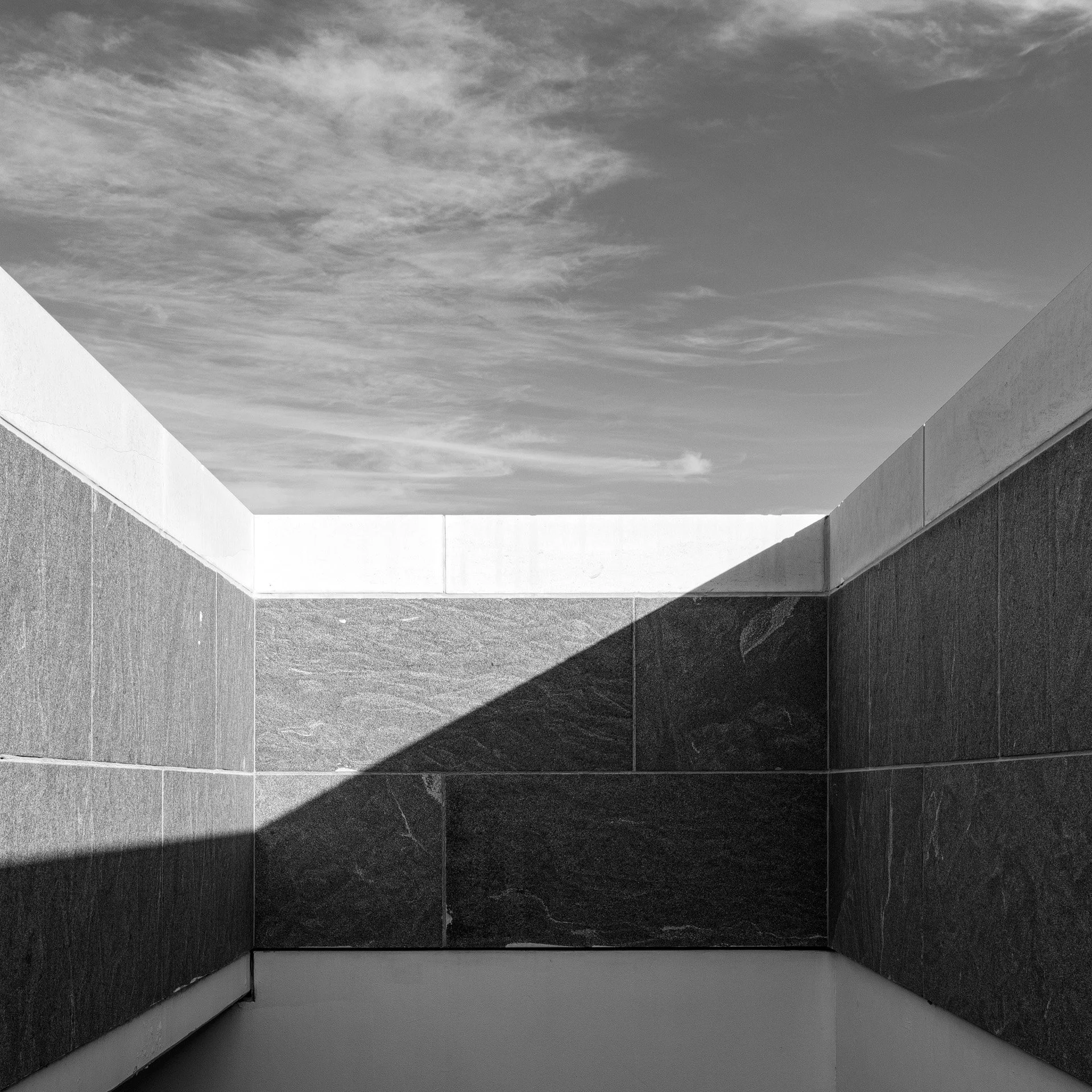 Low-angle black and white abstract photo looking up from the Museum of Islamic Art entrance stairwell showing granite walls and diagonal shadows by Hammad Iqbal