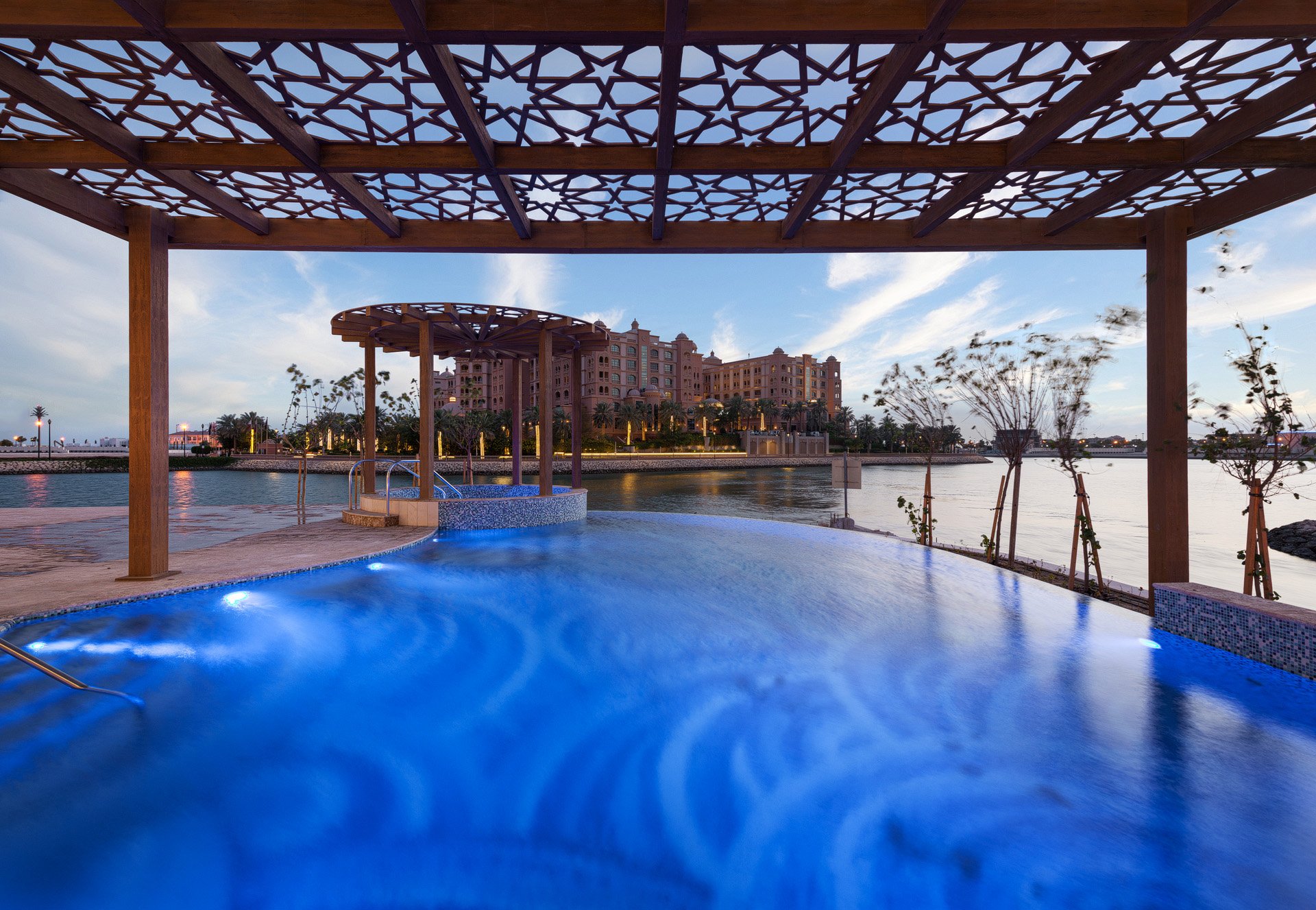Vibrant blue dusk photo of an illuminated infinity pool under a carved mashrabiya pergola with Marsa Malaz Kempinski in the background by Hammad Iqbal